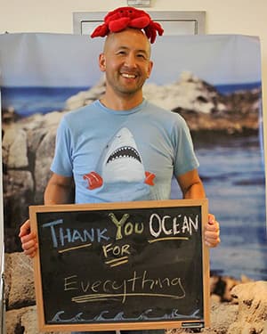 a person with a red crab on their head holding a sign that says thank you Ocean for Everything